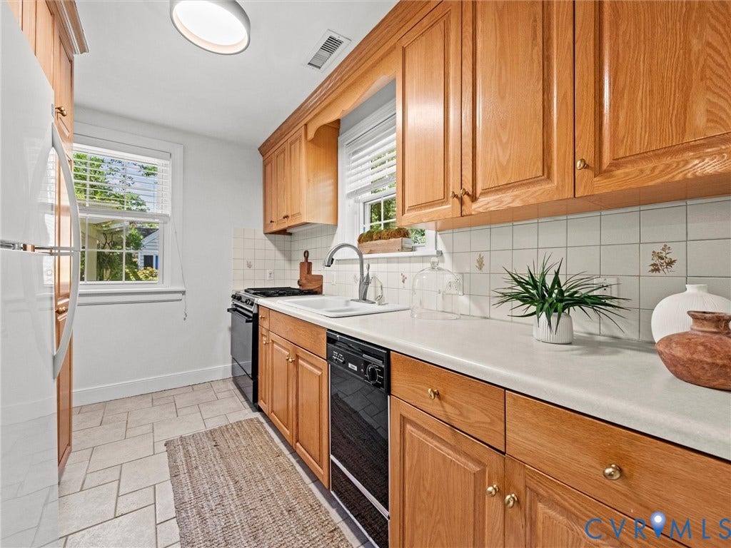 Hardwood cabinetry, white tile backsplash, white countertops, built-in dishwasher, and a window with blinds