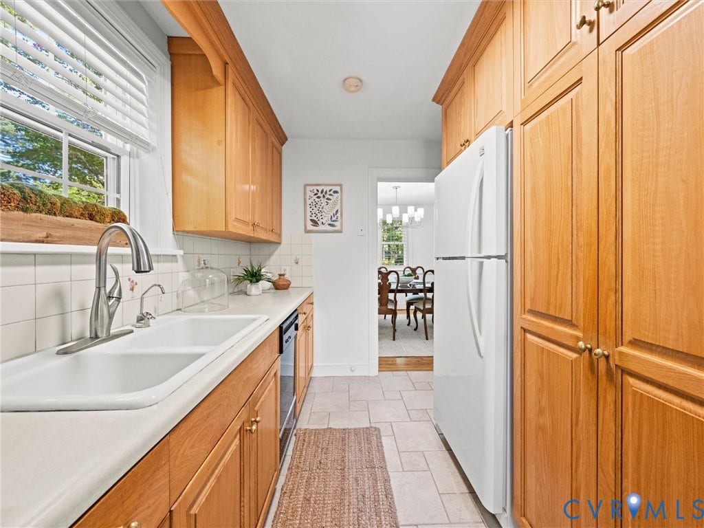 Galley-style kitchen with wood-finish cabinetry, tile flooring, and a double basin sink with a gooseneck faucet