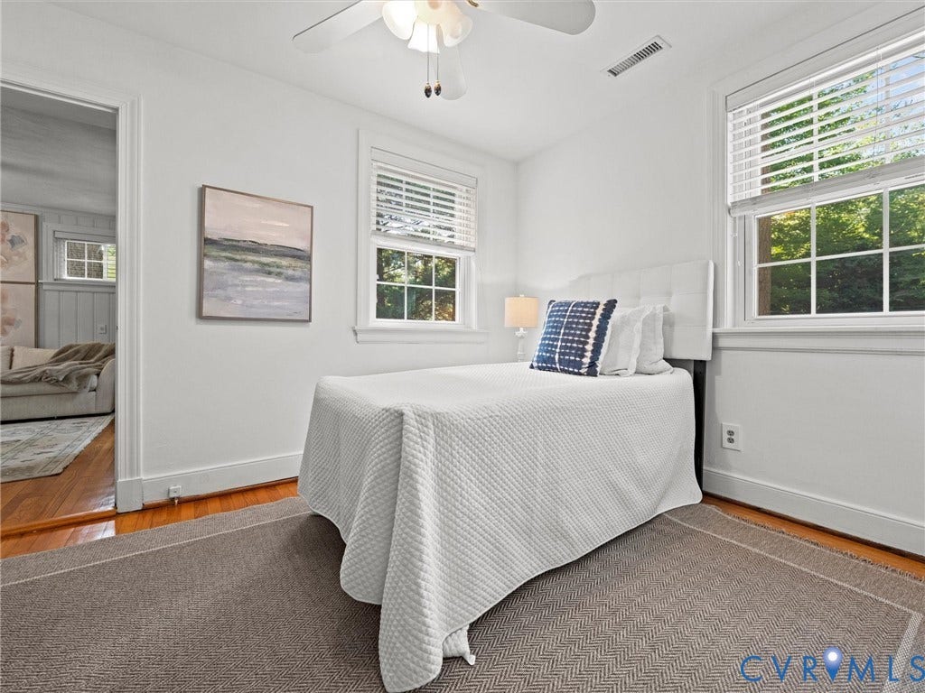 White walls, two windows with blinds, a white ceiling fan, and wood-finish flooring