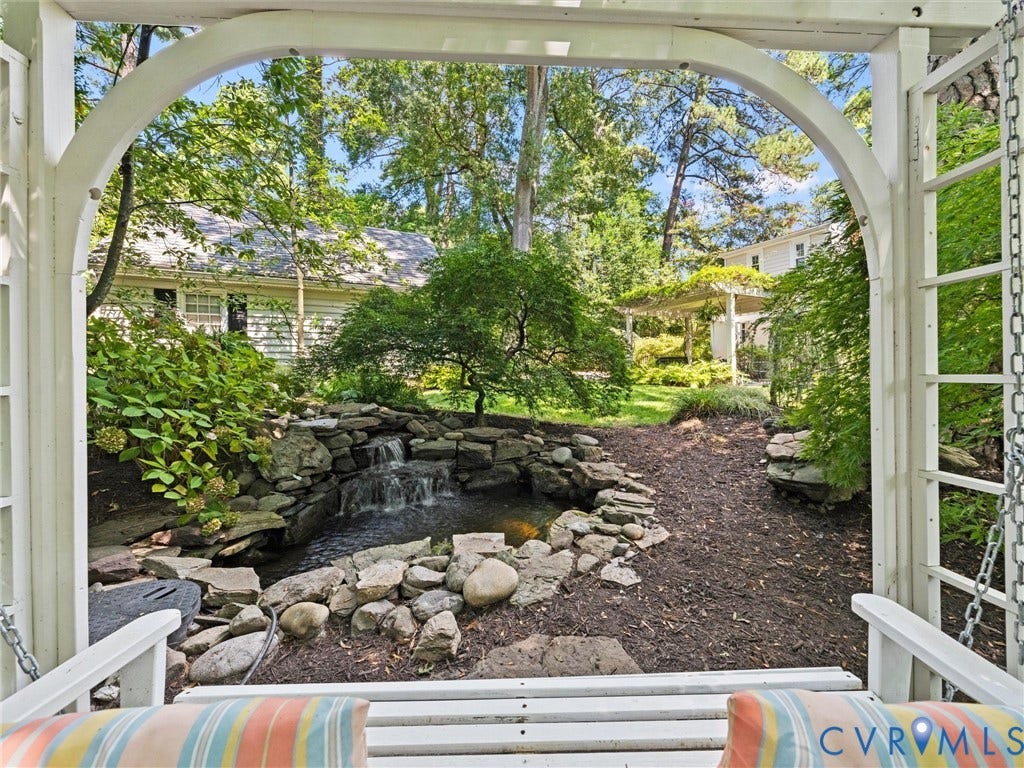 Backyard oasis featuring a tiered rock waterfall, mature landscaping, and a white pergola structure