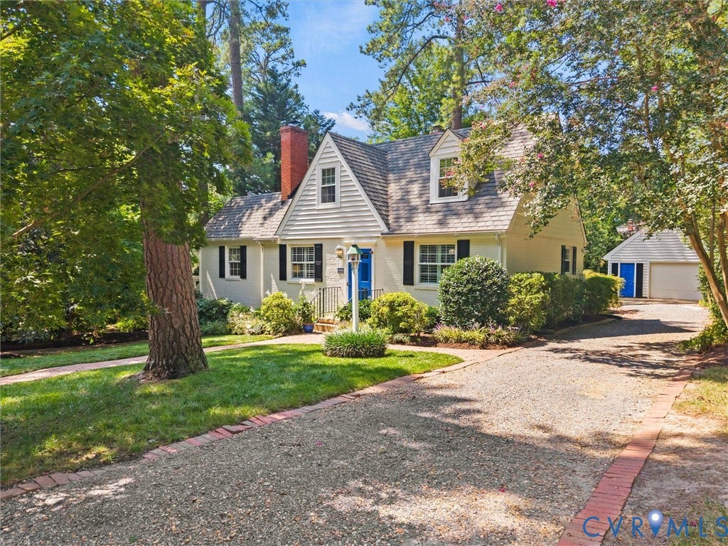 Dormer windows, a prominent brick chimney, and a gravel driveway with brick trim
