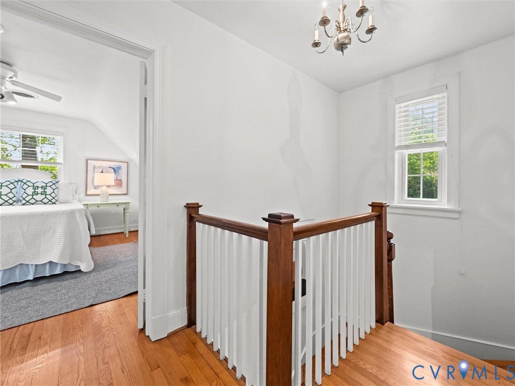 Hardwood flooring throughout, white walls, white window blinds, and an overhead chandelier