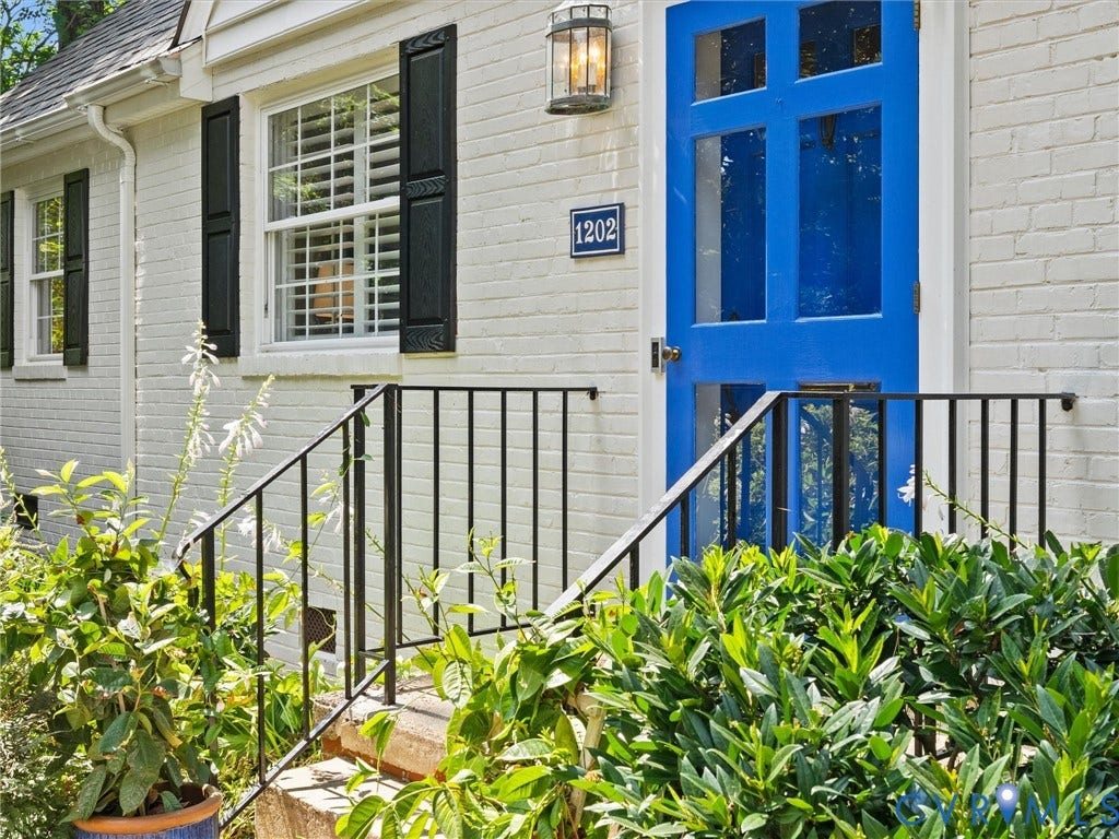 Brick exterior with white paint, vibrant blue entry door, black exterior shutters, and a black metal handrail