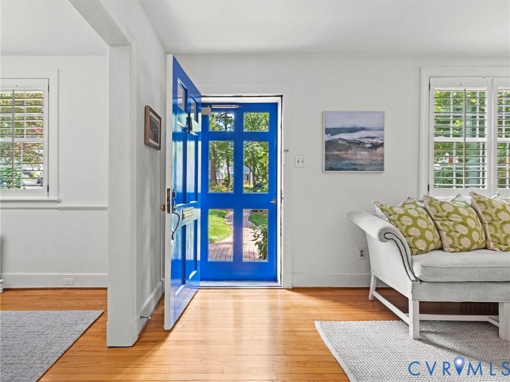 Vibrant blue paneled entry door, wood-finish flooring, white plantation shutters, and white wall finishes