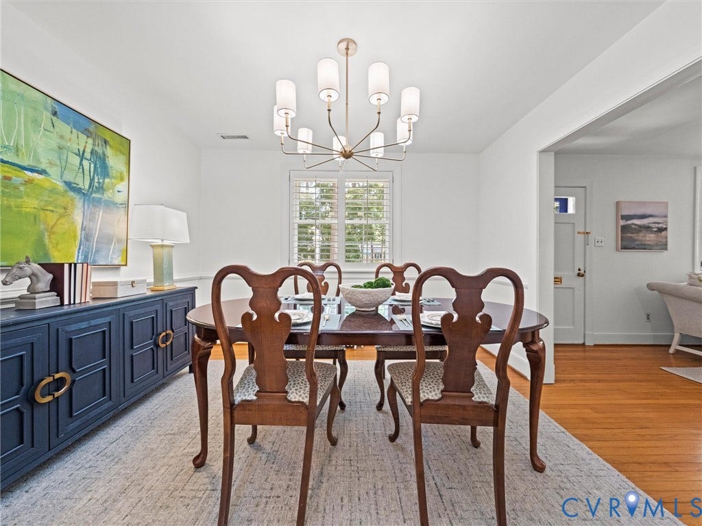 Dining area with hardwood flooring, a modern chandelier, and window shutters