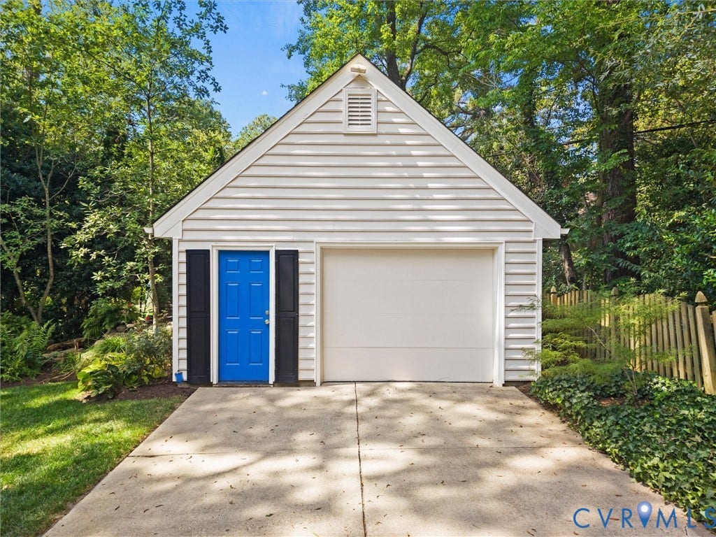 Detached garage with a single bay door, vibrant blue entry door, and dark shutters