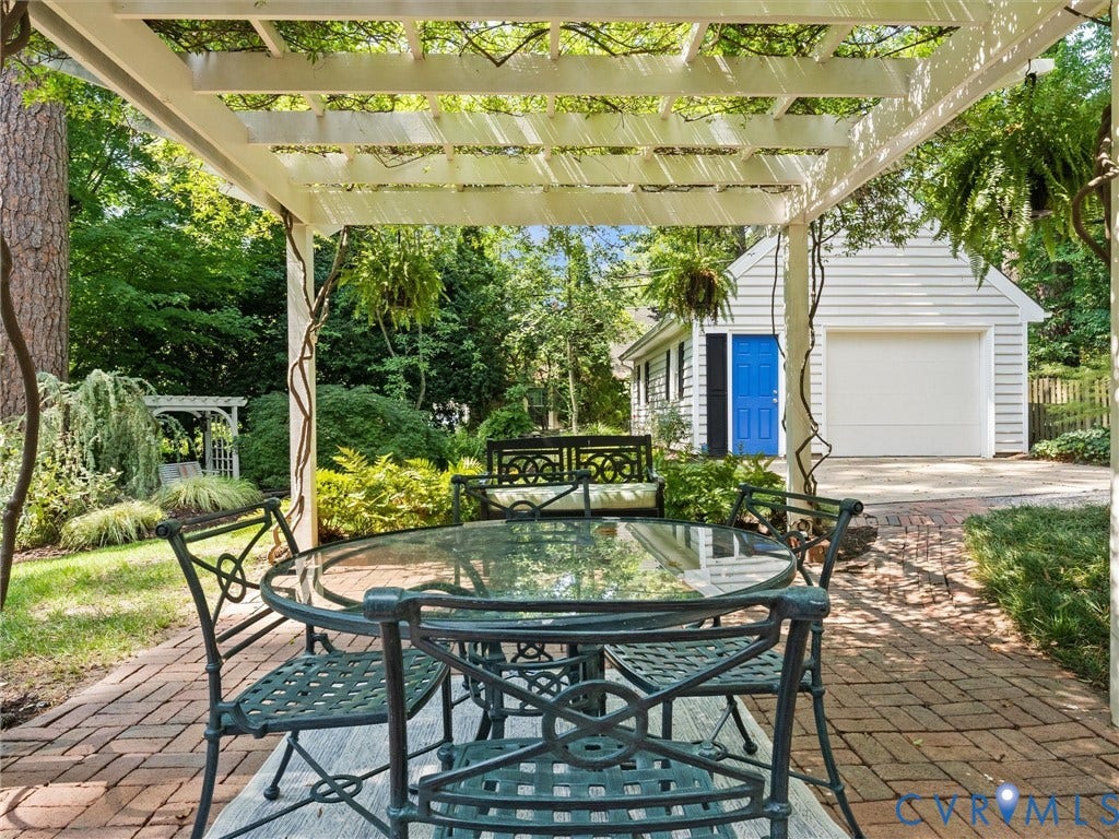 Pergola-covered brick patio with a detached garage and a white wooden swing arbor