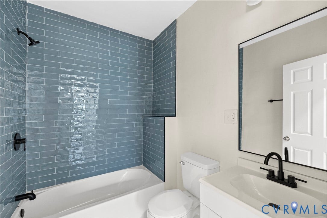 Bathroom featuring a white bathtub, blue subway tile surround, matte black fixtures, a white vanity with an integrated sink, and a framed mirror