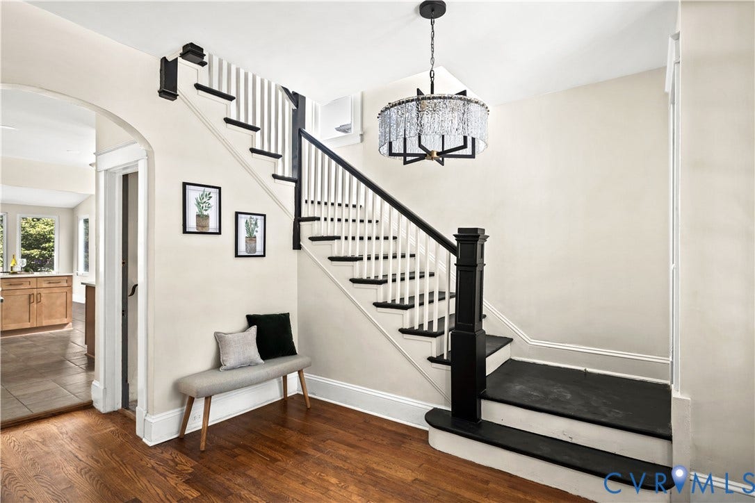 Hardwood flooring, painted staircase with white risers and black treads, black newel post and handrail, and an arched doorway