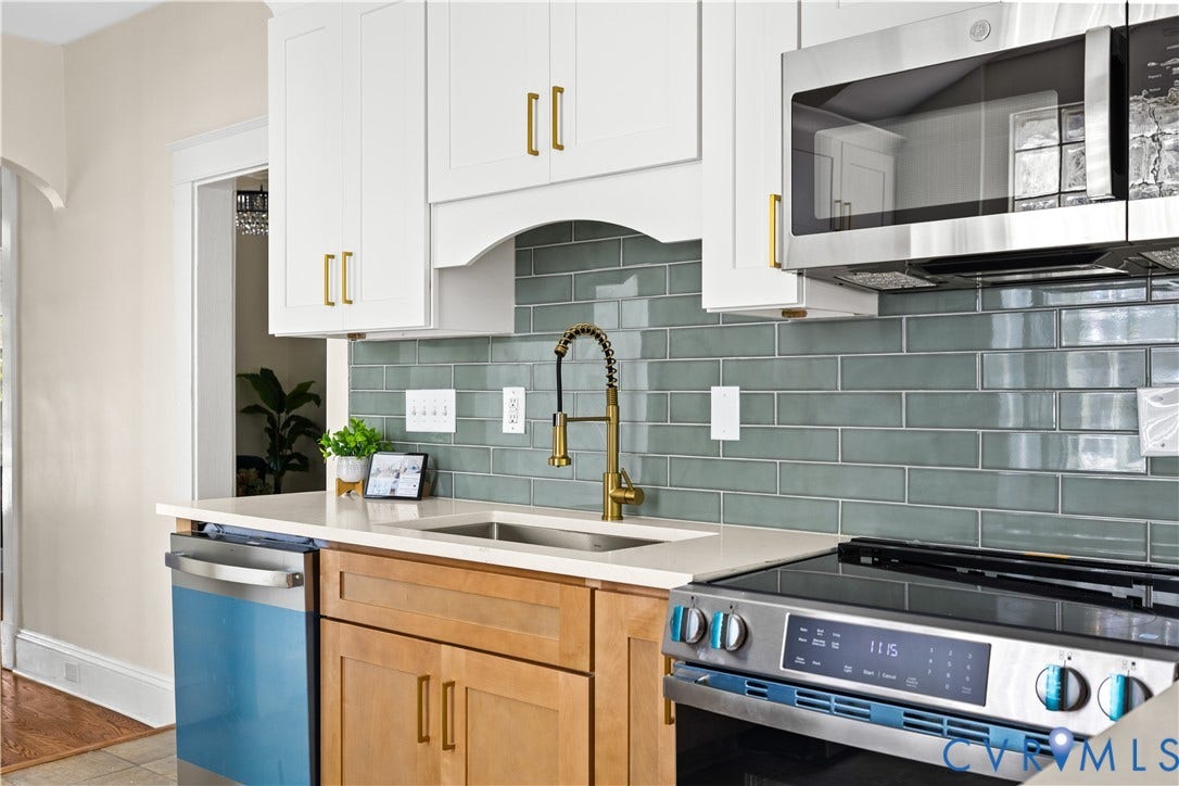 White upper cabinetry with gold-tone hardware, wood-finish lower cabinetry, light-toned countertop, subway tile backsplash, and stainless steel appliances