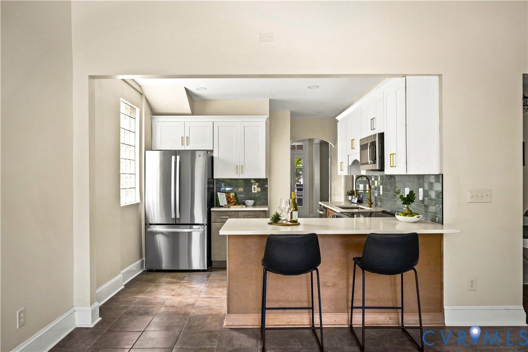Stainless steel refrigerator, white cabinetry, dark subway tile backsplash, light countertop, and a built-in microwave