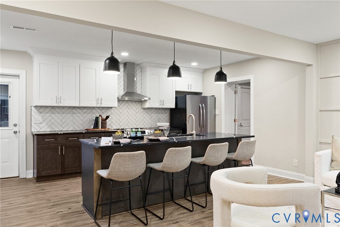 1500 Leicester Road, Cedarhurst - Westover Hills, Richmond, VA 23225 Kitchen featuring a dark-toned island with integrated seating, white shaker-style upper cabinetry, dark-toned lower cabinetry, stainless steel appliances, and a herringbone tile backsplash