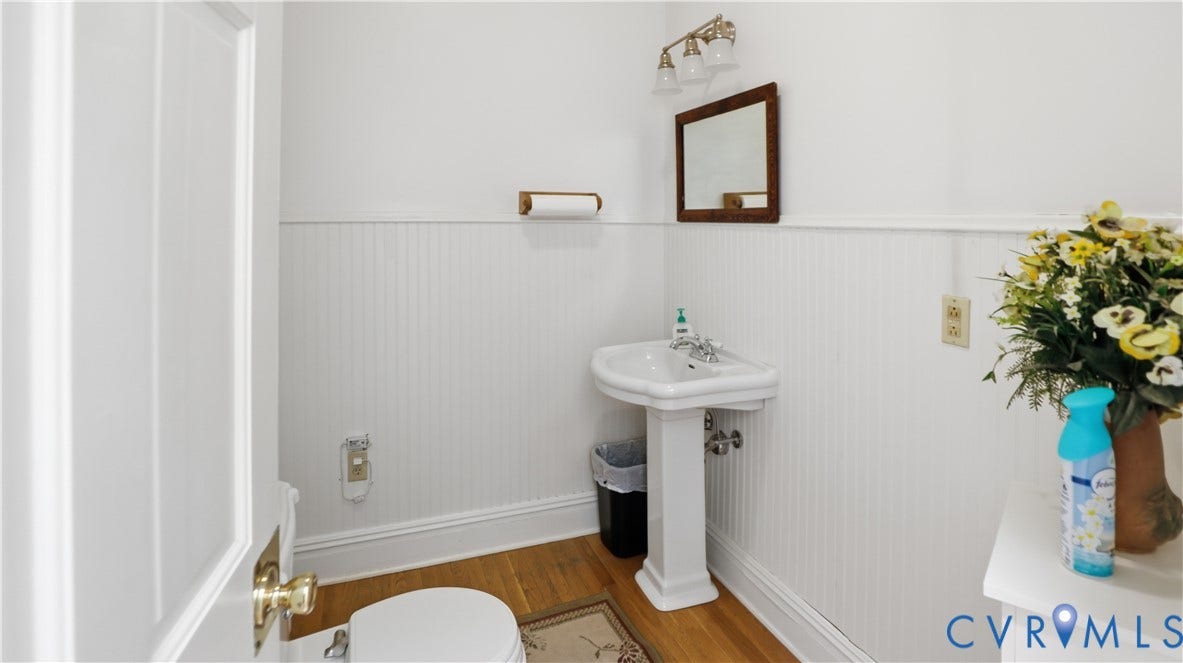 111 N 17th Street, Richmond, VA 23219 Pedestal sink with chrome fixtures, wood-finish flooring, white beadboard wainscoting, and a wall-mounted mirror