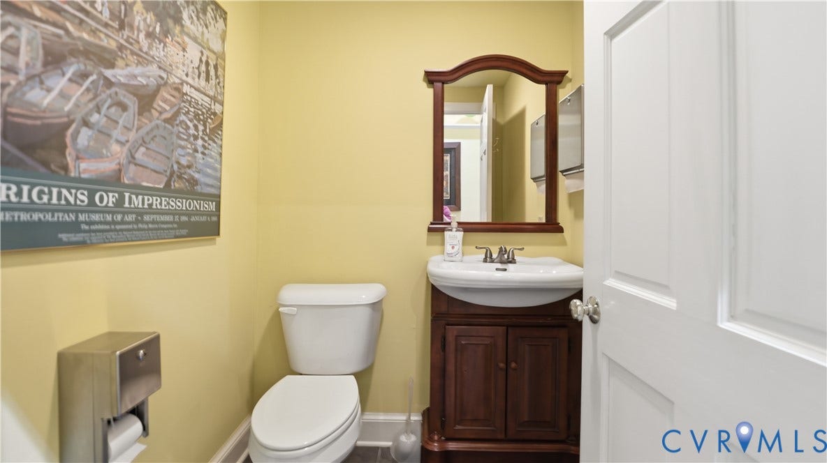 111 N 17th Street, Richmond, VA 23219 White toilet, wood-finish vanity with a white basin sink, and a wood-finish framed mirror