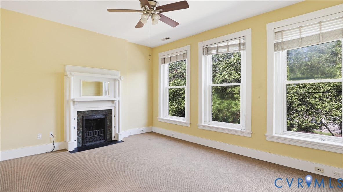 111 N 17th Street, Richmond, VA 23219 Spacious room featuring three large windows, a decorative fireplace with a dark stone surround, a ceiling fan, and light-colored carpeting