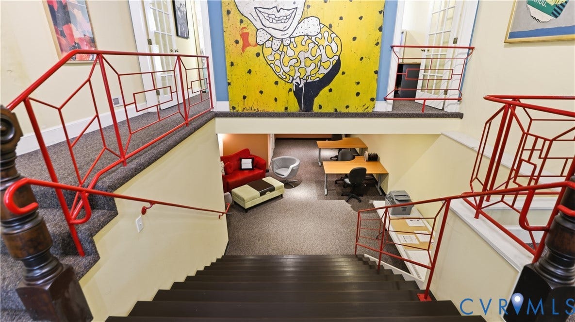 111 N 17th Street, Richmond, VA 23219 Multi-level interior featuring a carpeted staircase with dark wood-finish treads and risers, red geometric metal railings, and a lower-level carpeted space