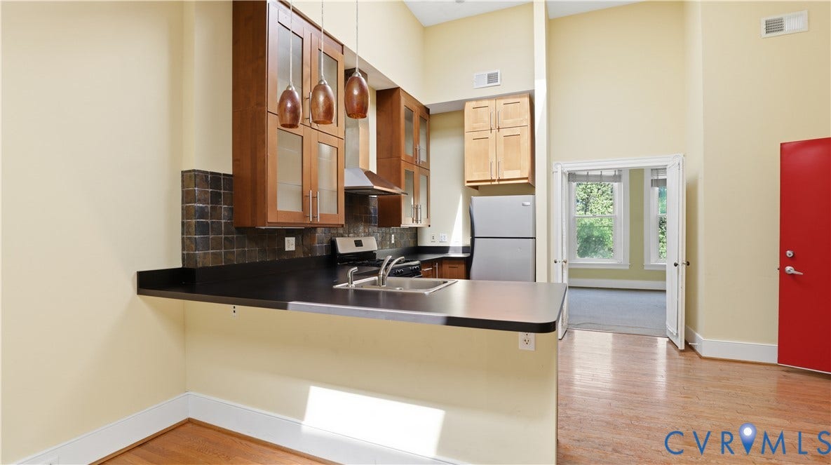111 N 17th Street, Richmond, VA 23219 Kitchen featuring a breakfast bar, dark countertops, a stainless steel sink, and wood cabinetry with glass accents