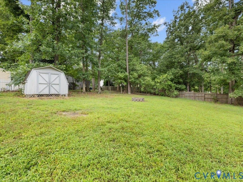 3313 New Found Lane, Chester, VA 23831 Expansive lawn surrounded by mature trees, featuring a storage shed and a stone fire pit