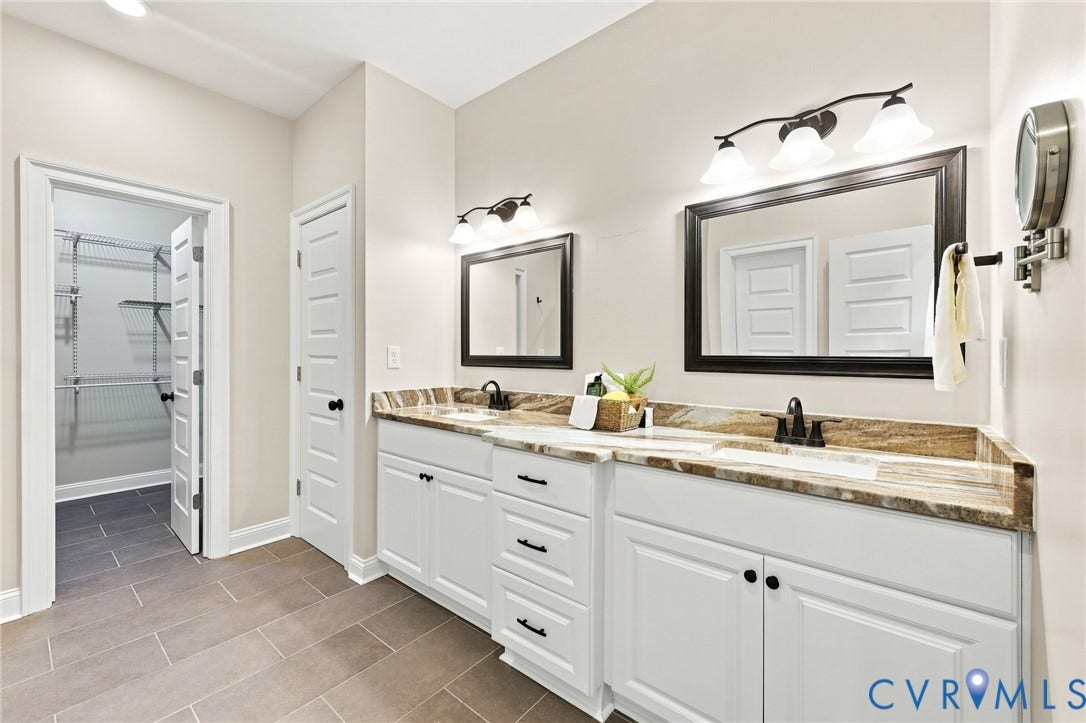 Spacious primary bath features separate vanities, granite countertops, tile flooring, and direct access to the walk-in closet.