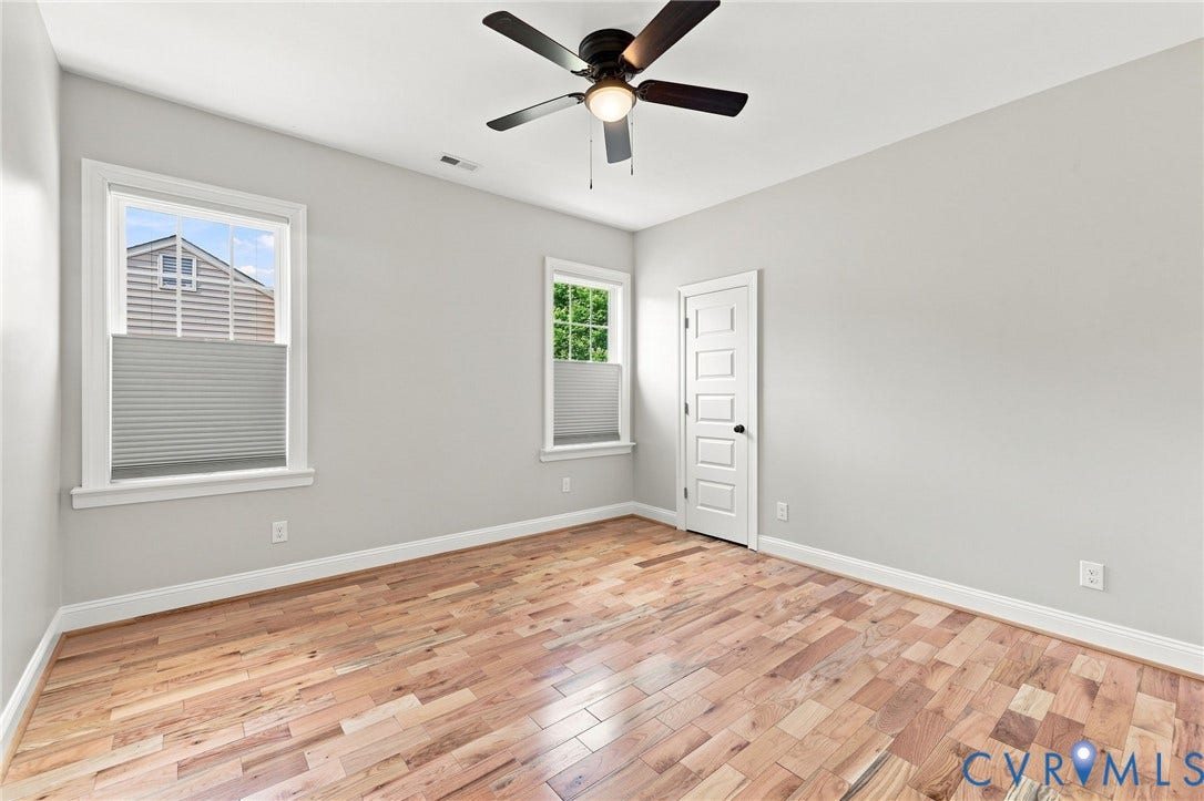 Spacious fourth bedroom with hardwood floors, ceiling fan, two windows, and fresh neutral paint.