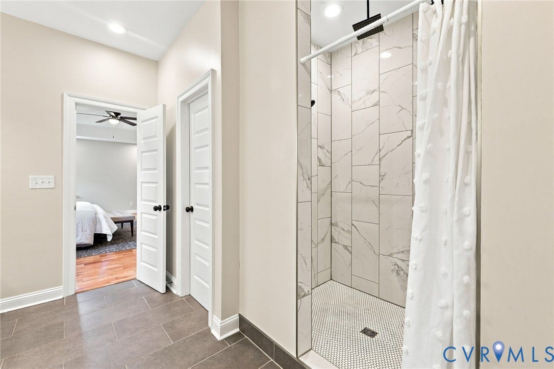 Oversized walk-in shower features floor-to-ceiling tile, a rainfall showerhead, and modern black fixtures.