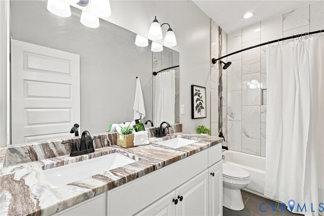 Well-appointed hall bath offers a double vanity, granite countertops, tile flooring, and a tiled tub/shower surround.