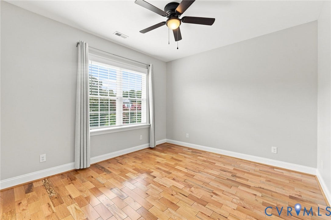 Bright freshly painted third bedroom with hardwood floors, ceiling fan, large window, and ample closet space.