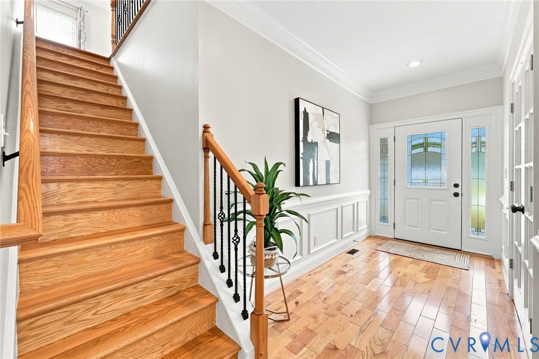 Bright, inviting foyer with hardwood floors, detailed molding and wainscoting, plus a beautiful hardwood staircase with iron balusters.