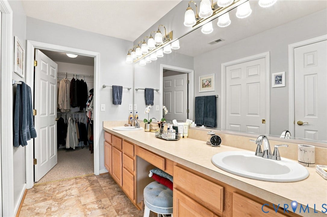 7230 Norwood Pond Court, Midlothian, VA 23112 Dual vanity with integrated sinks, wood cabinetry, large mirror, and adjacent walk-in closet with built-in shelving