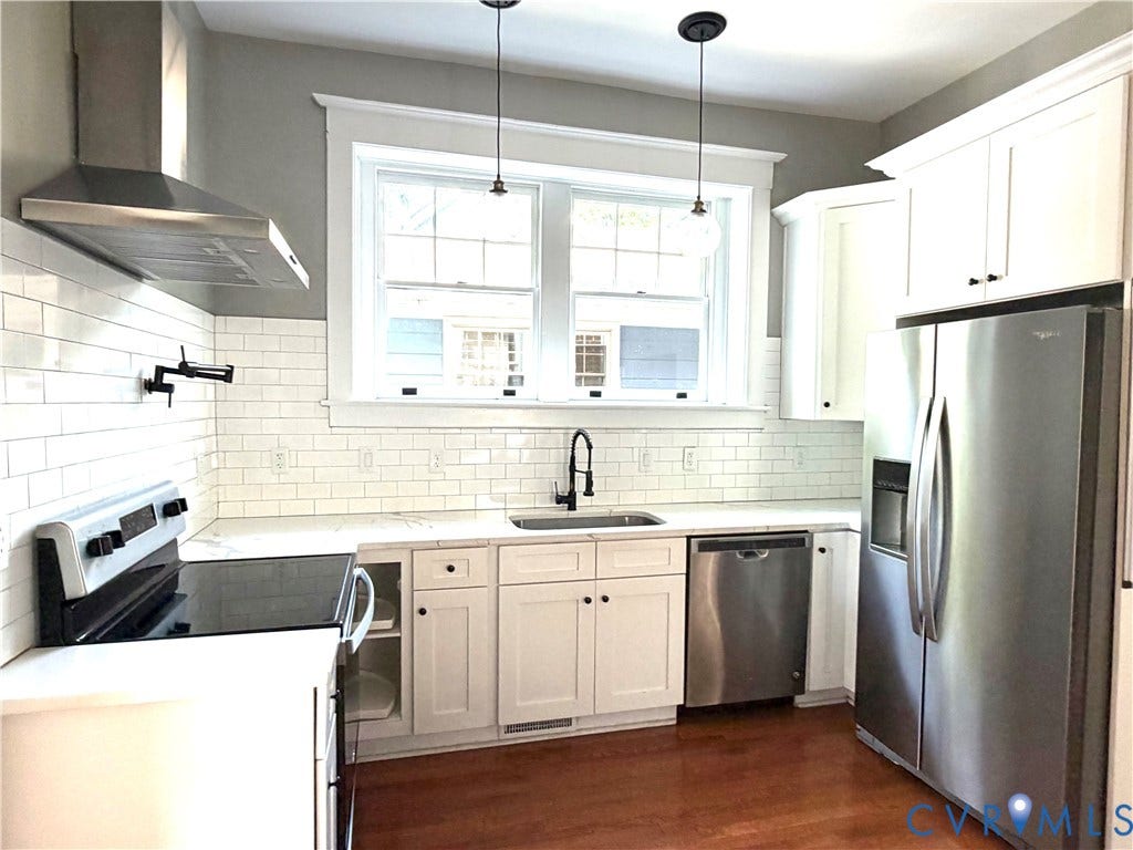 3614 Carolina Avenue, Richmond, VA 23222 White subway tile backsplash, white cabinetry, stainless steel appliances, wood-finish flooring, and pendant lighting