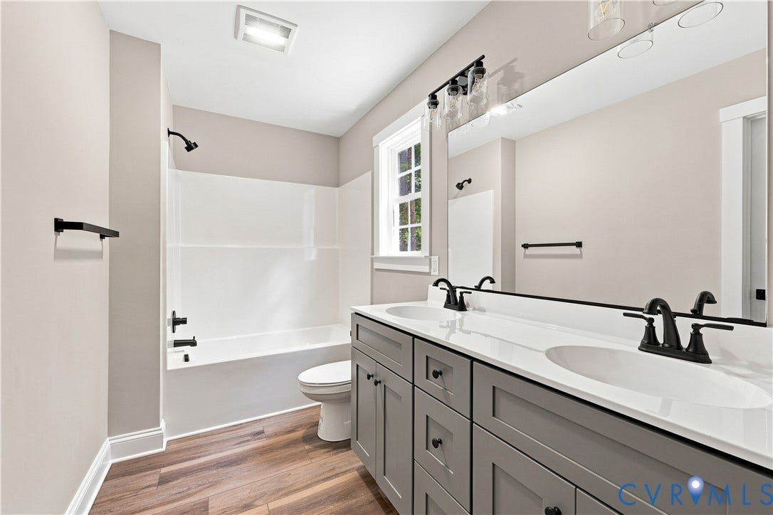 42 Clinton Farm Court, Clinton Farm, Cumberland, VA 23040 Dual vanity with undermount sinks and matte black fixtures, full-width mirror, wood-finish flooring, and white tub/shower combination