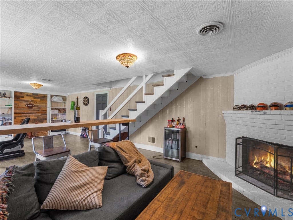 Brick fireplace with a hearth, wood-finish flooring, built-in shelving, paneled accent wall, and a staircase
