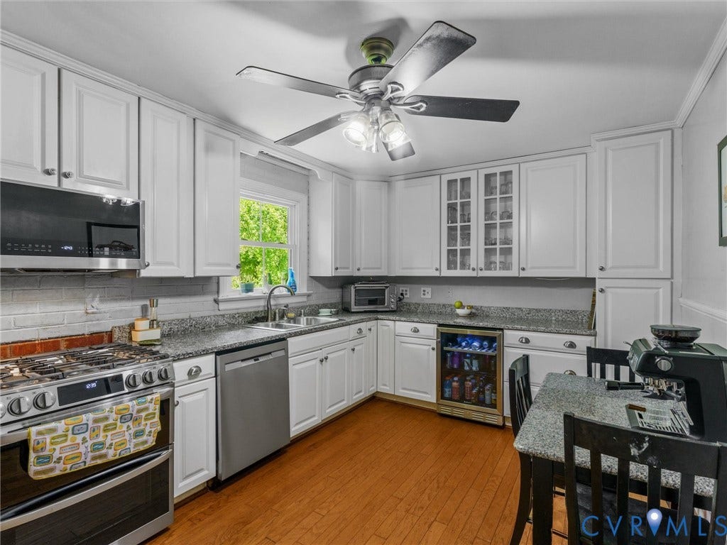 White cabinetry, granite countertops, stainless steel appliances, wood-finish flooring, and built-in beverage cooler