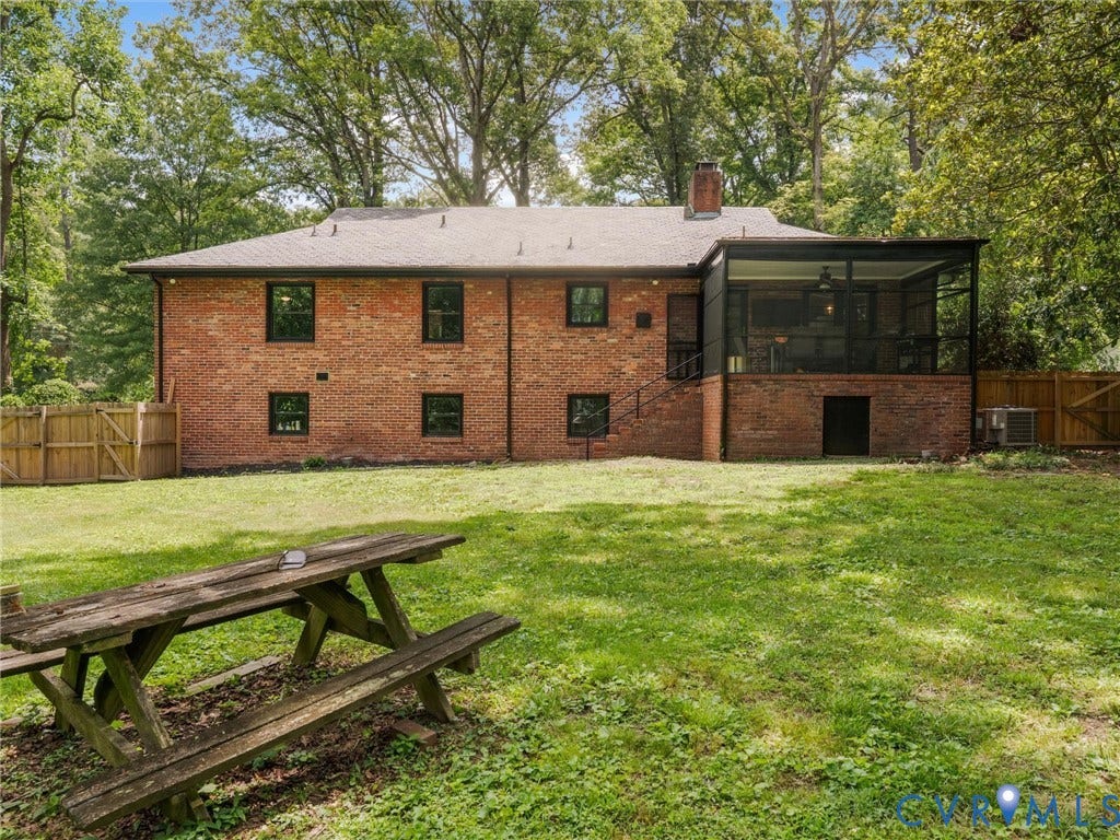 Brick exterior with black-framed windows, screened-in porch with ceiling fan, rear entry door with black railings, and a fenced yard