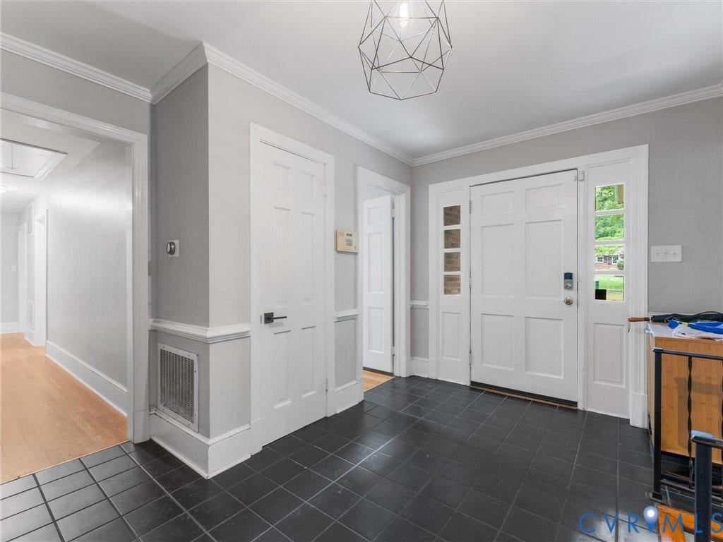 Entryway featuring dark tile flooring, white panel doors, decorative trim work, and a modern geometric light fixture