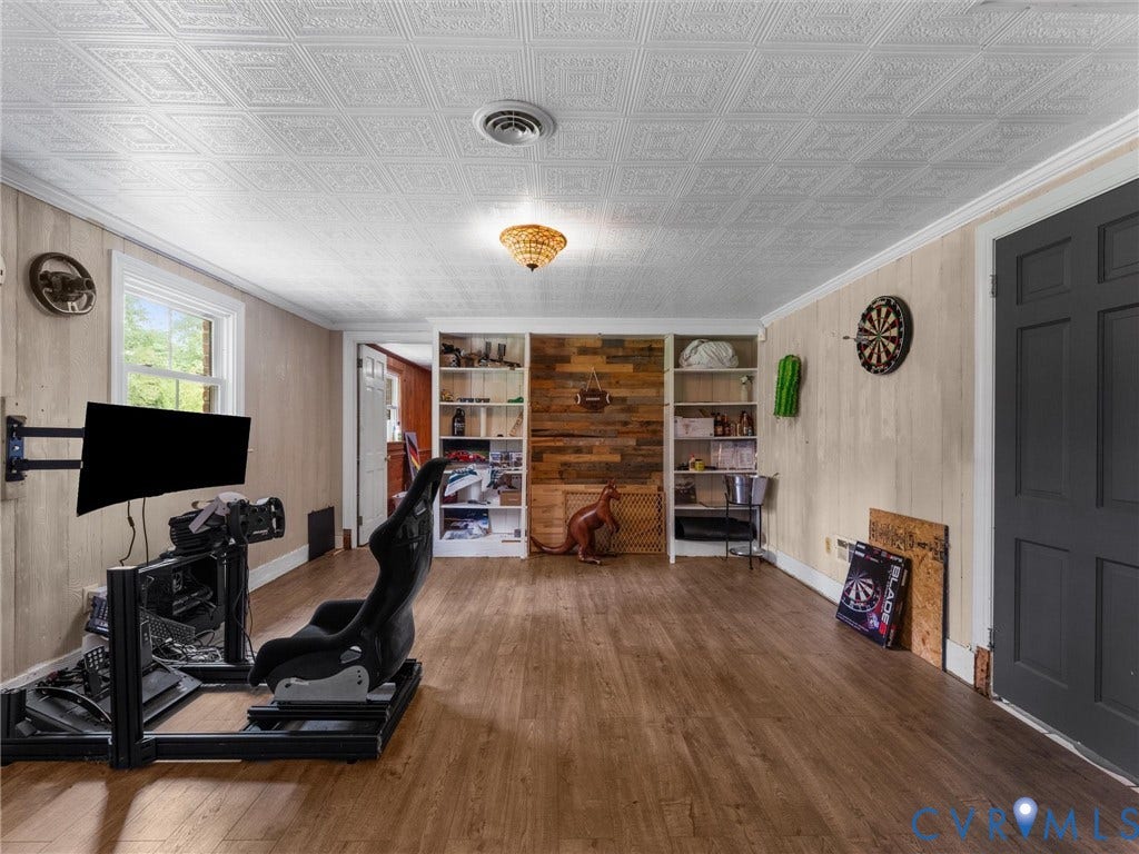 Wood-finish flooring, white paneled walls, white window trim, and a patterned ceiling with a central light fixture