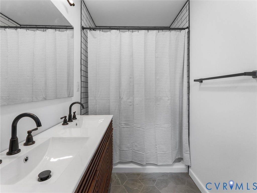 Double vanity with integrated sinks, dark bronze fixtures, slatted wood-finish cabinetry, and hexagonal floor tiling