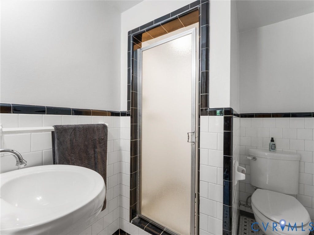 White subway tile with black trim, a wall-mounted sink, and a shower with a frosted glass door
