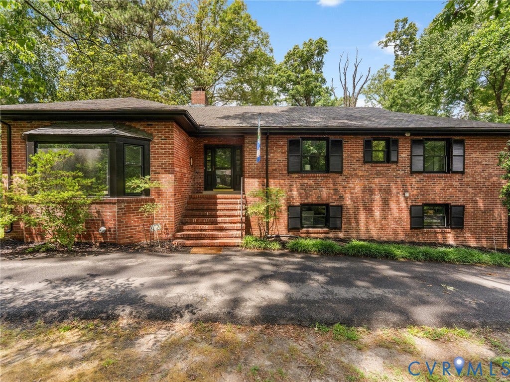 Brick exterior with a prominent bay window, black framed windows, black window shutters, a front entry door with glass panels, and brick steps with handrails