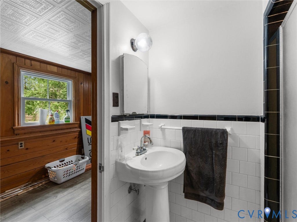 Pedestal sink with chrome fixtures, white tile wainscoting, and black accent tile