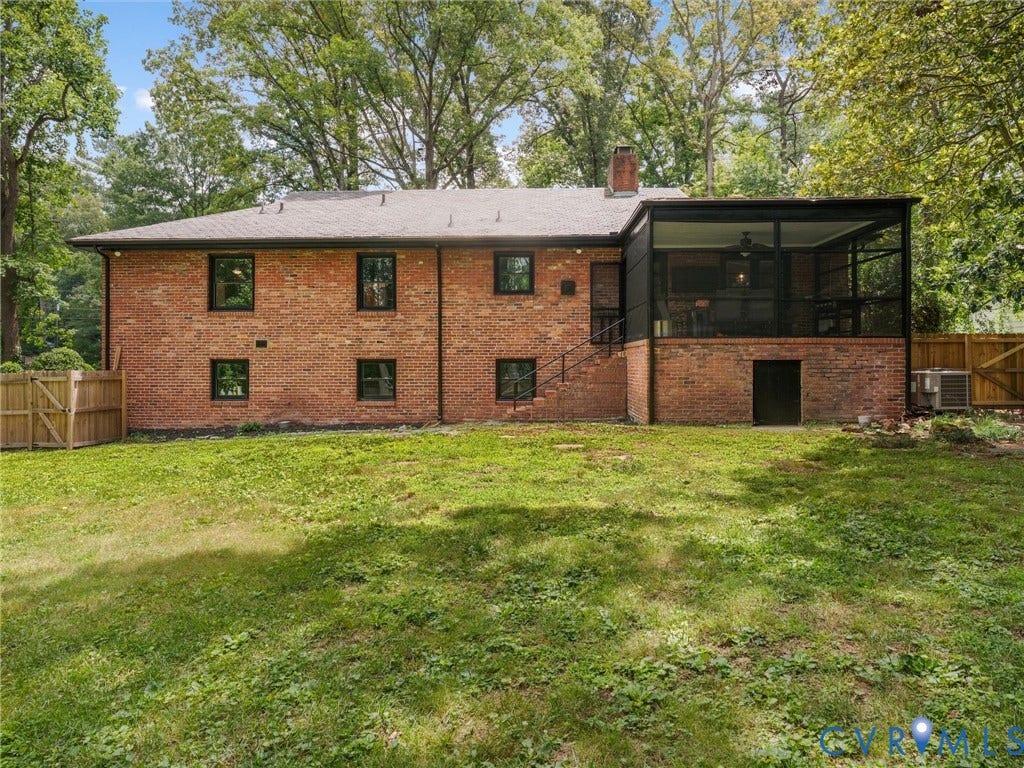 Brick exterior with black-framed windows, screened porch with ceiling fan, exterior staircase, and mature trees