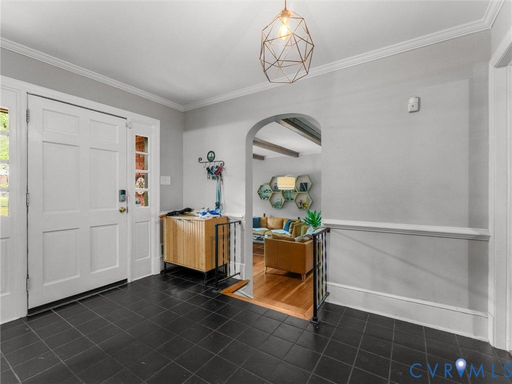 Entryway featuring dark square tile flooring, a white paneled door with sidelight, an arched doorway, and a geometric pendant light fixture