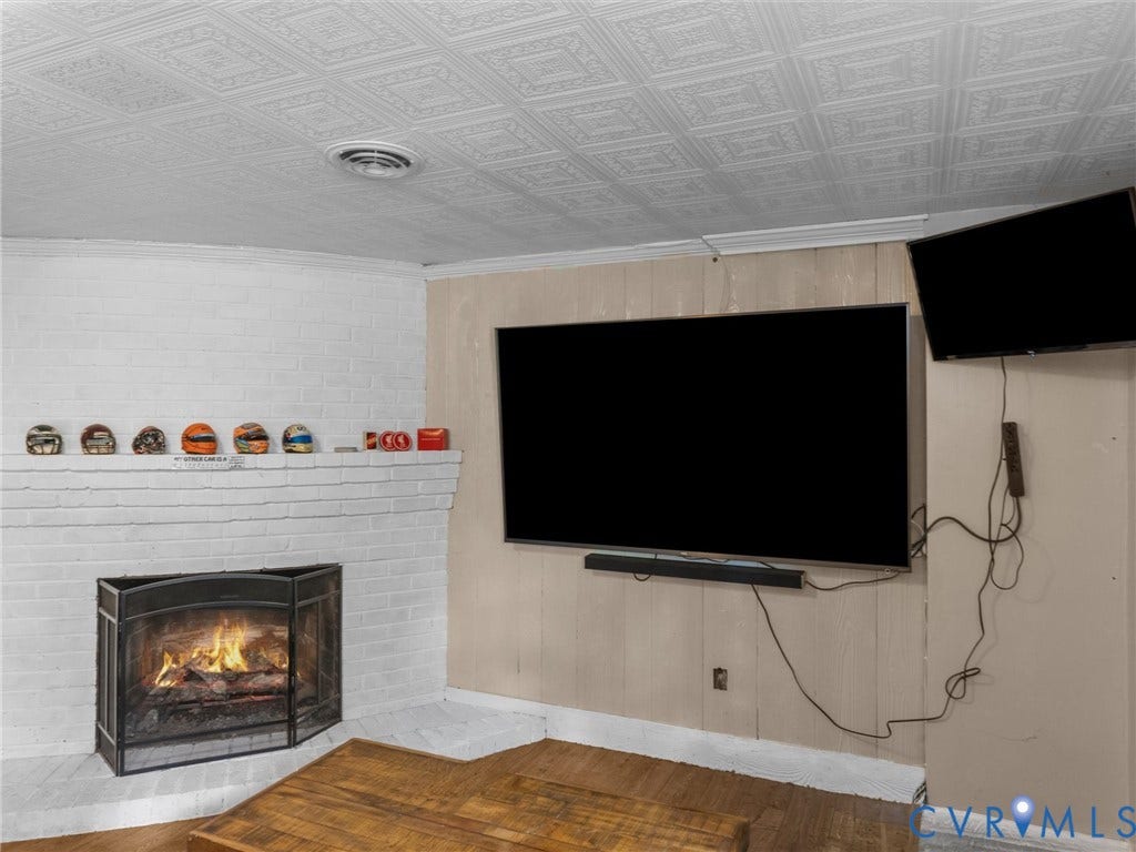Painted brick fireplace with metal screen, wood-finish flooring, and a patterned ceiling