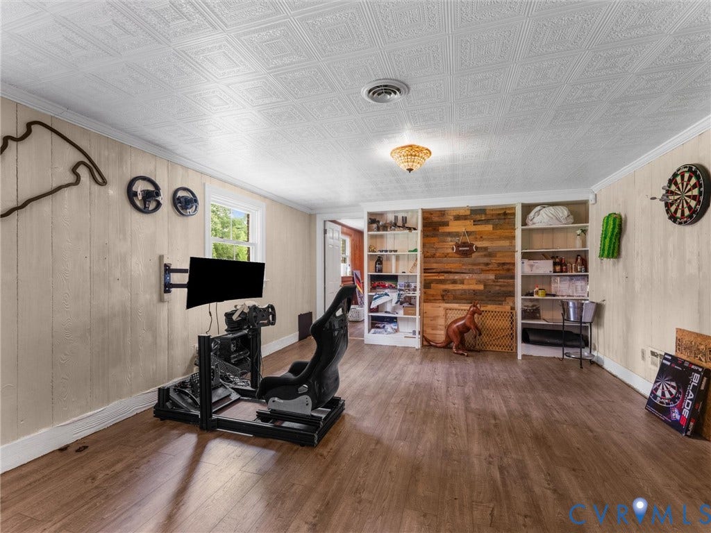 Wood-finish flooring, white wood paneling, decorative ceiling, built-in shelving, and a chandelier-style light fixture