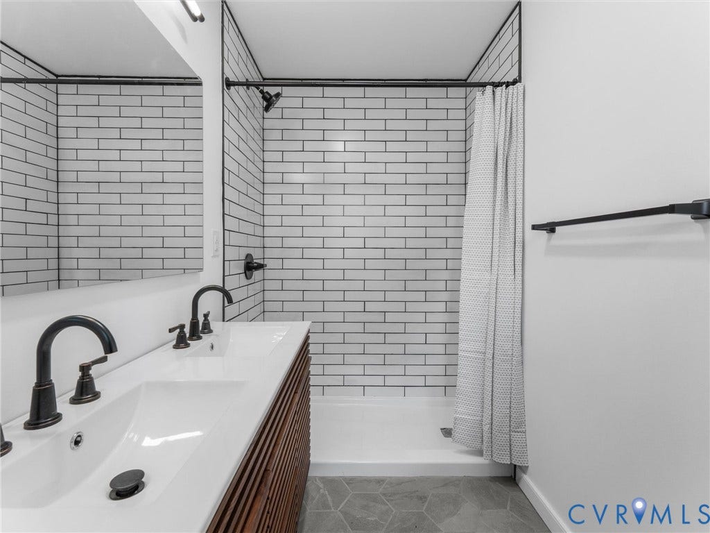 Modern bathroom featuring subway tile walls, a double vanity with wood-finish cabinetry and rectangular vessel sinks, matte black faucetry and hardware, and a walk-in shower with glass enclosure and rainfall showerhead