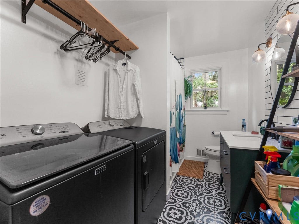 Laundry area with a built-in wood shelf and hanging rod, complemented by a full bathroom featuring patterned floor tiles, a window, and a vanity with a white countertop