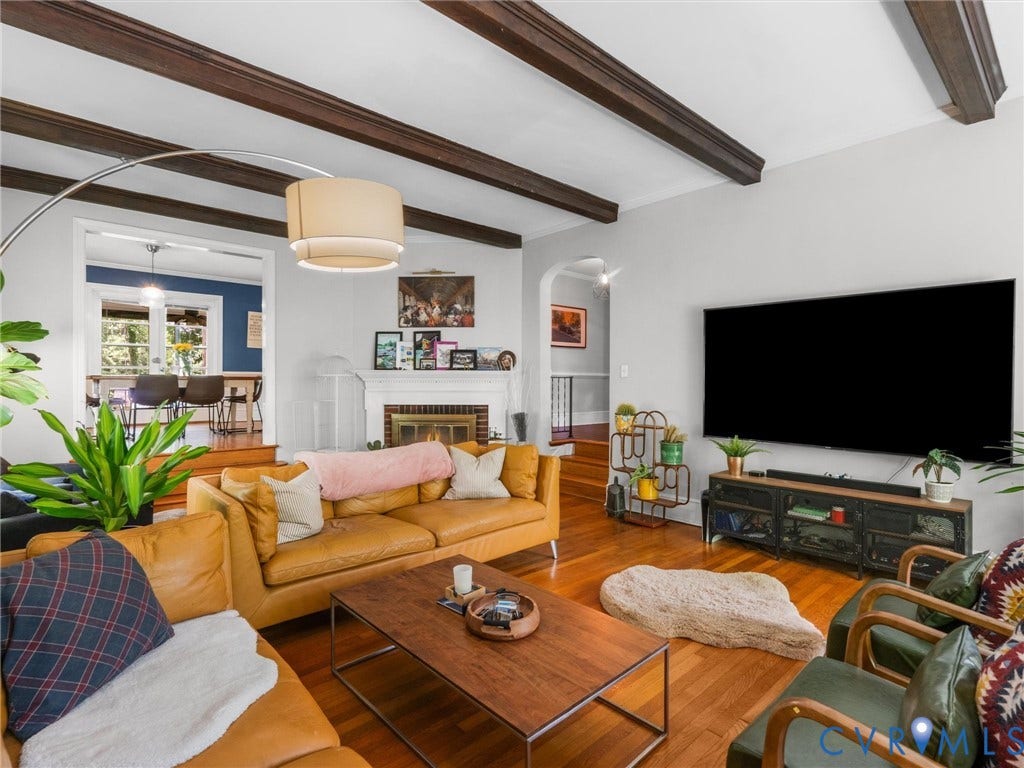 Living room featuring wood-finish flooring, exposed ceiling beams, a white fireplace with a mantel, and an arched doorway
