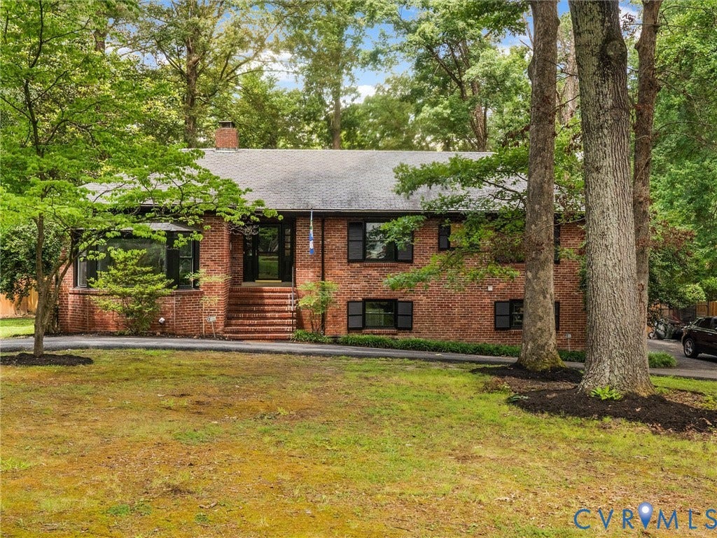 Brick exterior with a dark shingle roof, featuring multiple windows with dark shutters, and a prominent front entrance with brick steps