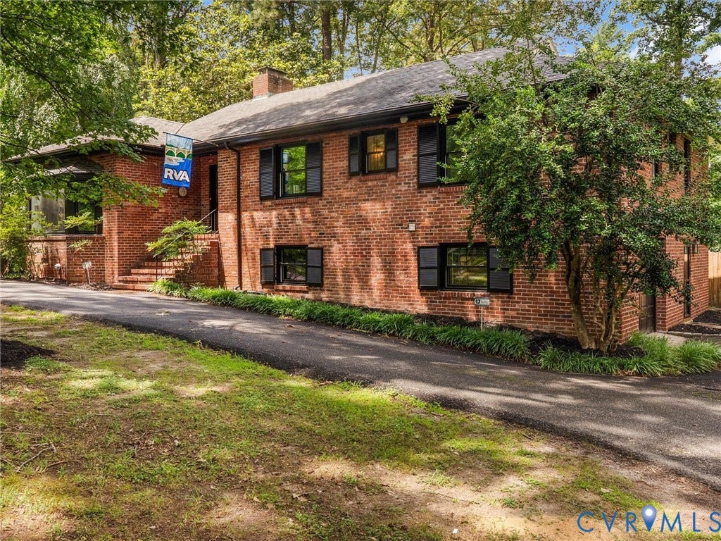 Brick exterior, black shutters, asphalt driveway, mature trees, landscaped shrubbery