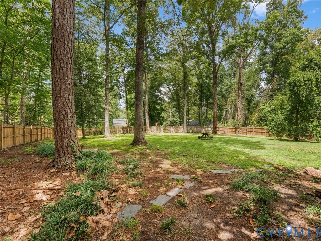 Expansive backyard with a manicured lawn, established trees, and a full privacy fence